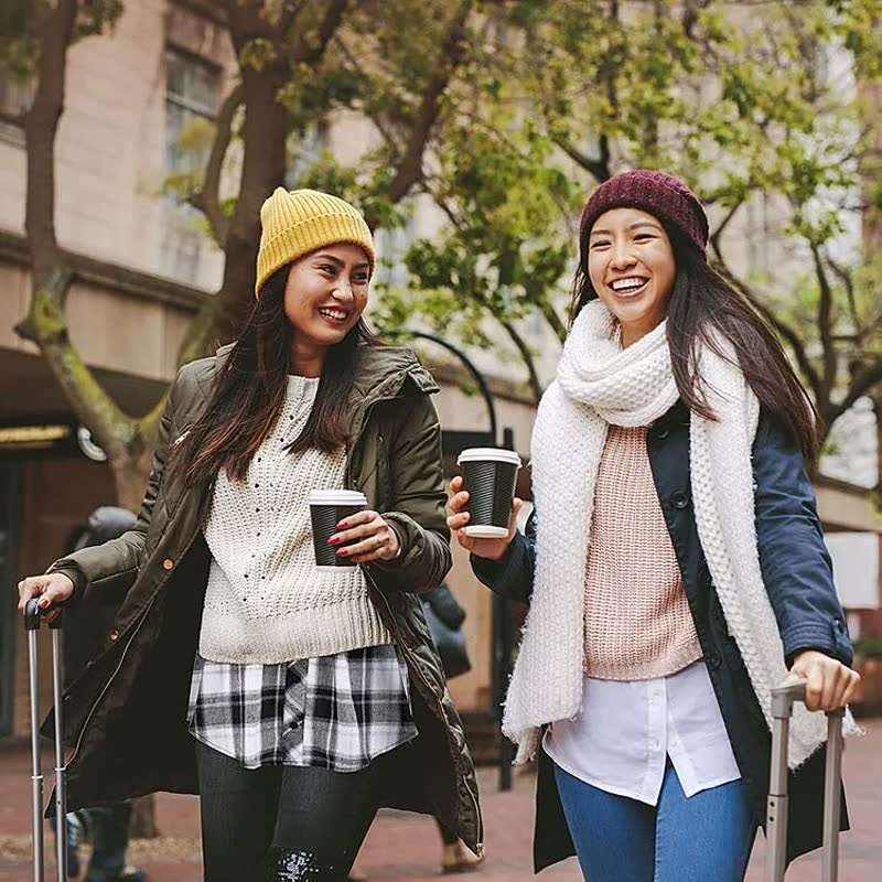 Zwei Frauen in Winterkleidung mit Kaffeebechern, lächelnd, draußen spazierend.