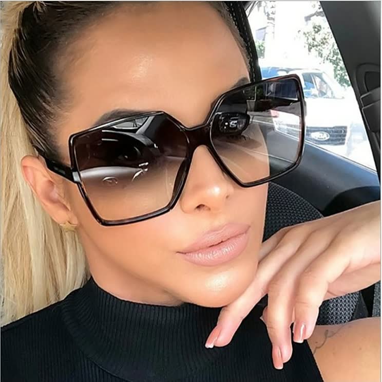 Frau mit übergroßer, eckiger Sonnenbrille, schwarzes Gestell, modisches Accessoire.