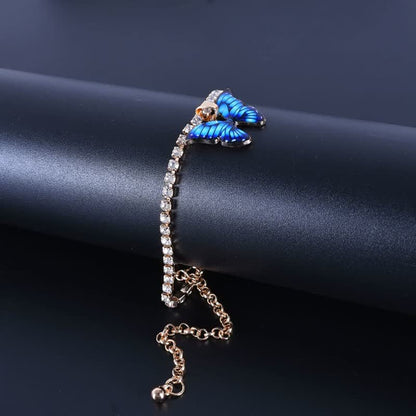 Goldenes Armband mit blauen Schmetterlingen und Strasssteinen auf schwarzem Hintergrund.