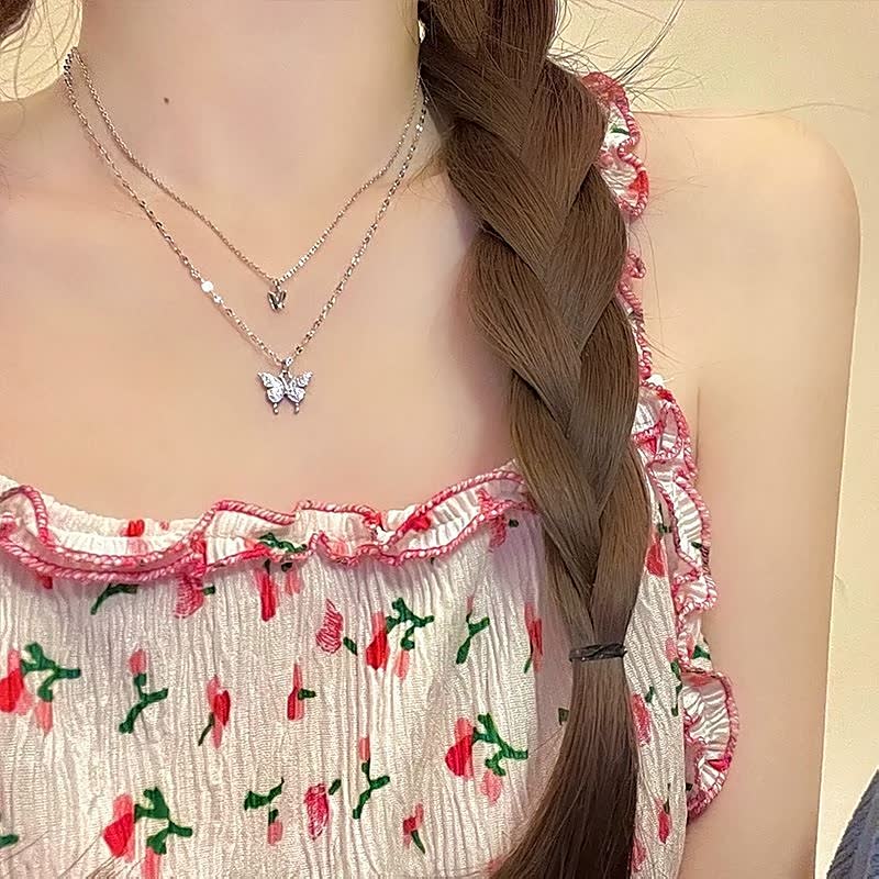 Frau mit geflochtenem Haar trägt silberne Schmetterlingskette und geblümtes Sommerkleid.