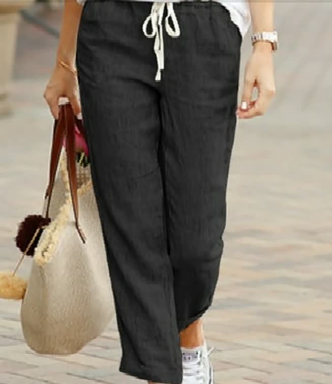 Frau in schwarzer Leinenhose mit Kordelzug, hält eine Strohtasche, lässiger Sommerlook.