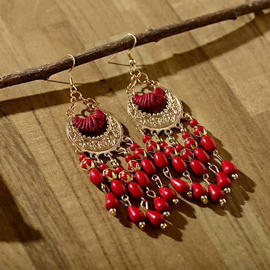 Goldene Ohrringe mit roten Perlen, handgefertigt, Boho-Stil, hängend auf Holzoberfläche.