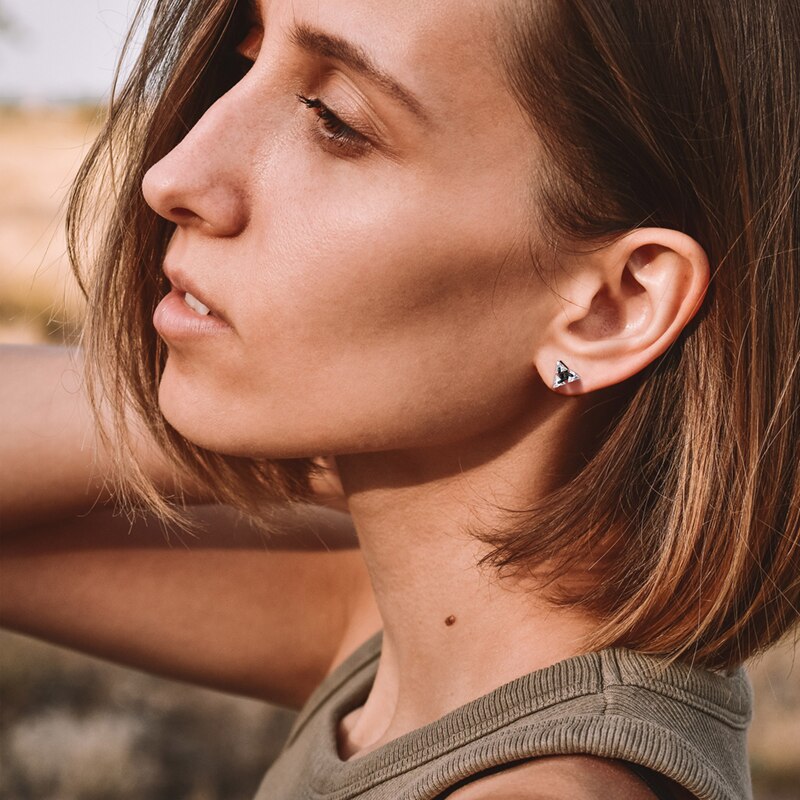 Frau mit silbernem Dreieck-Ohrring, kurze braune Haare, grünes Top, im Freien.