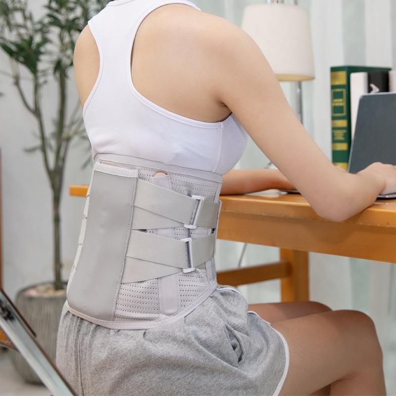 Frau trägt grauen Rückenstützgürtel, sitzt am Tisch, ergonomische Haltung, Rückenschmerzen Linderung.