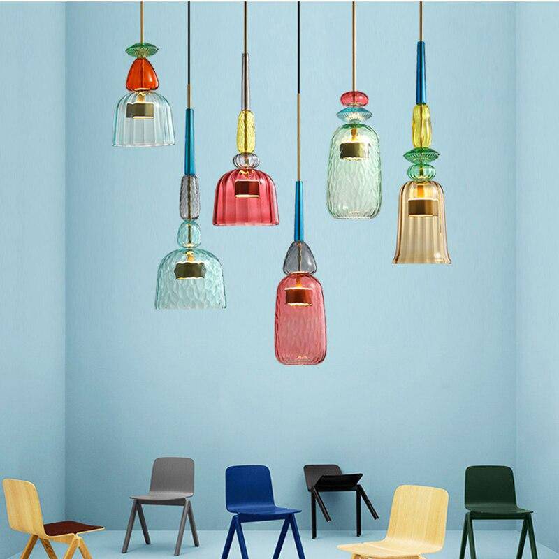Bunte Glas-Pendelleuchten in modernem Design, hängend in einem Raum mit bunten Stühlen.