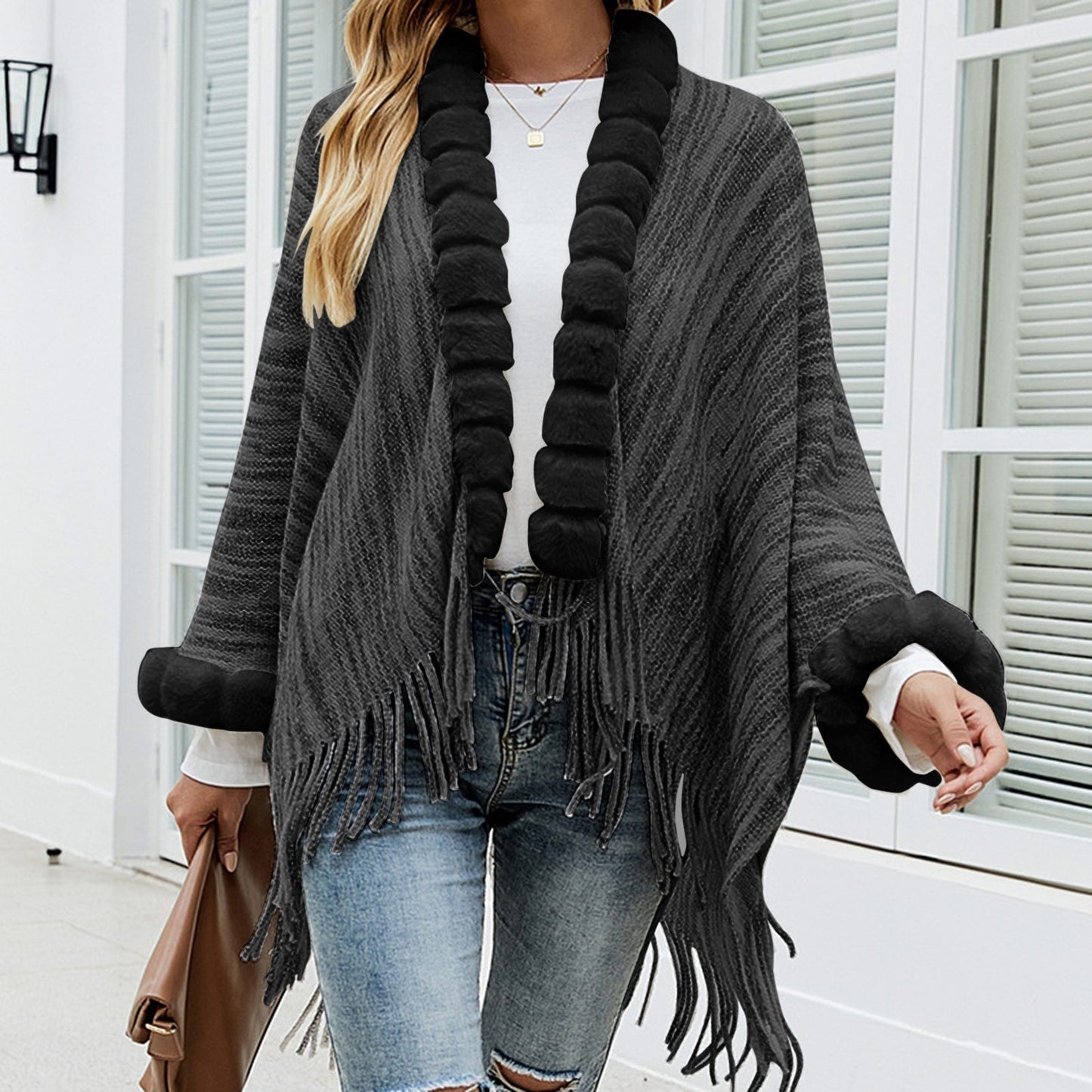 Frau trägt grauen Poncho mit Fransen, Strickmuster, schwarzem Kragen, modisch, elegant.