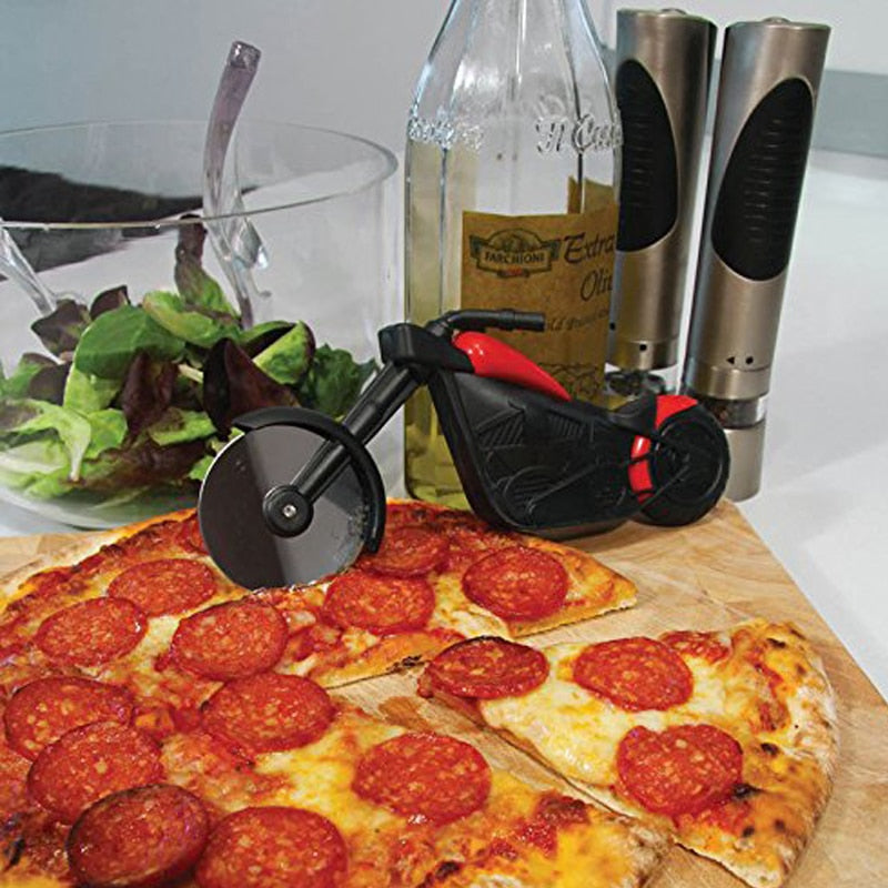 Motorrad-Pizzaschneider schwarz-rot, neben Salat und Pfeffermühlen auf Holzbrett.