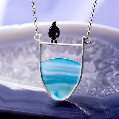 Silberkette mit blauem Achat-Anhänger und schwarzem Vogel, eleganter Schmuck für Damen.