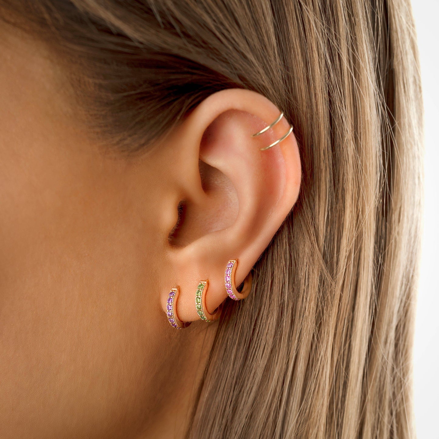 Frauenohr mit drei goldenen Creolen, rosa und grün, modische Ohrringe, Schmucktrends.