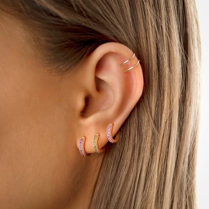 Frauenohr mit drei goldenen Creolen, rosa und grün, modische Ohrringe, Schmucktrends.
