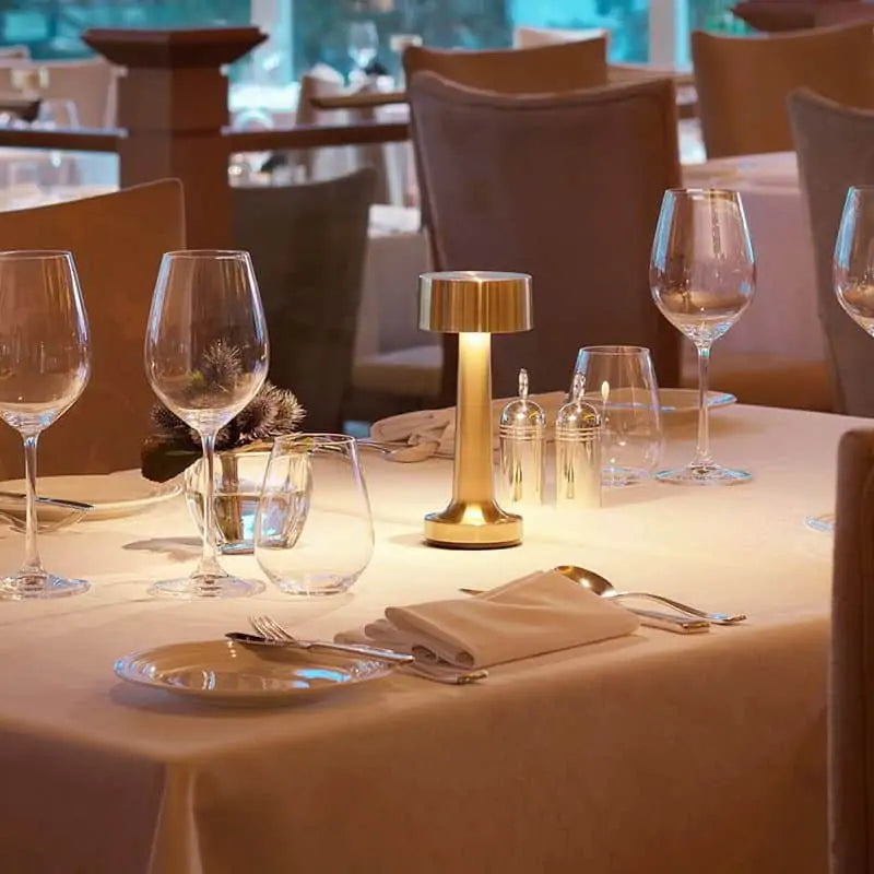 Eleganter Esstisch mit goldener Tischlampe, Weingläsern und weißem Tischtuch im Restaurant.