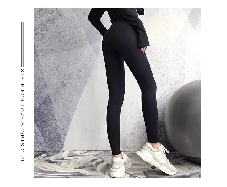 Frau in schwarzer Sportleggings und weißen Sneakers vor grauem Hintergrund.