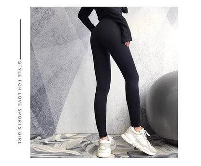Frau in schwarzer Sportleggings und weißen Sneakers vor grauem Hintergrund.