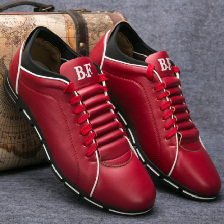 Rote Herrenschuhe aus Leder mit Schnürsenkeln, stilvoll, vor Reisetasche platziert.
