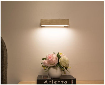Drehbare LED-Wandleuchte aus Holz, beleuchtet, über Vase mit Rosen auf Tisch.