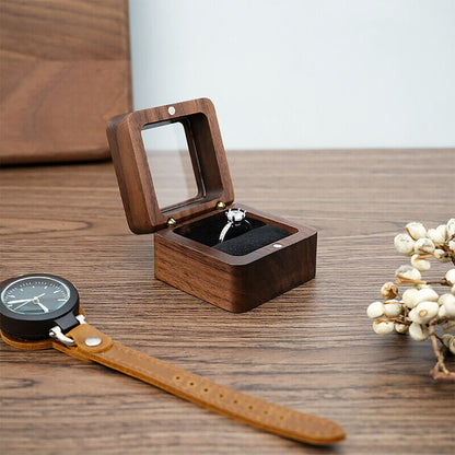 Offene Holzuhrbox mit Ring, daneben eine Armbanduhr auf Holztisch, elegantes Design.