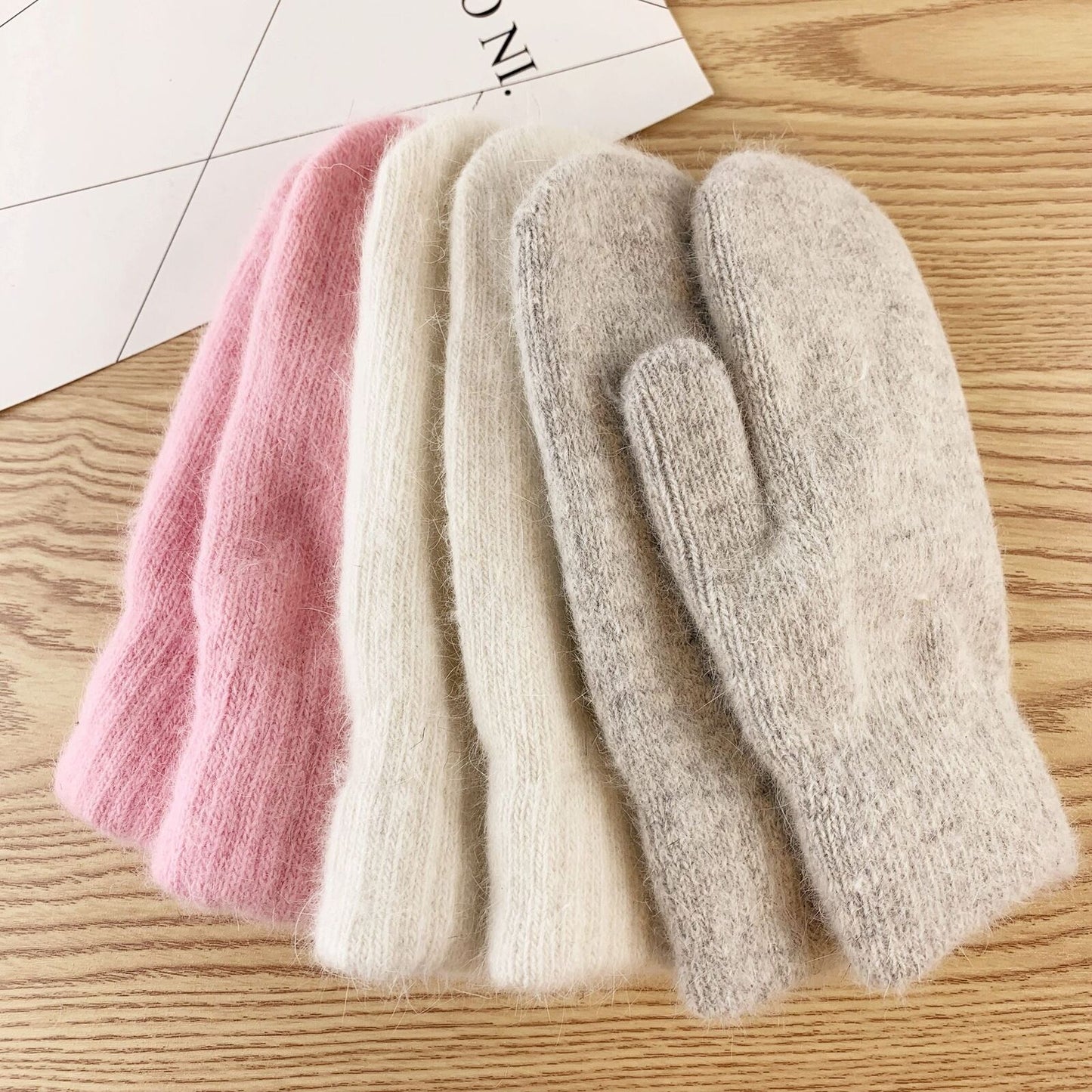 Vier gestrickte Wollhandschuhe in Rosa, Weiß und Grau auf Holztisch, Wintermode Accessoire.