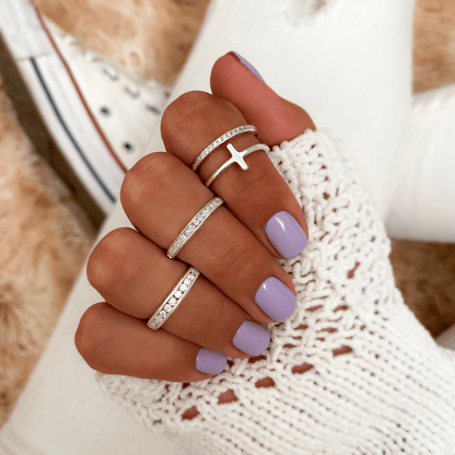Frau mit lila Nagellack trägt silberne Ringe, Kreuzdesign, gestrickter weißer Pullover.
