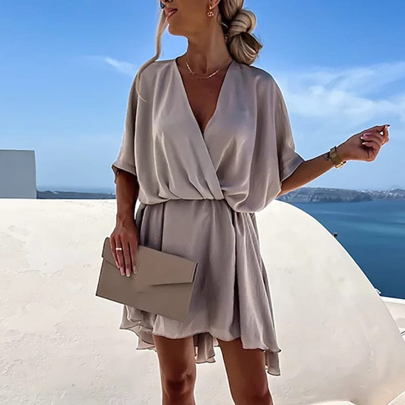Frau in elegantem, beigem V-Ausschnitt-Kleid, kurzärmelig, A-Linie, Strandkulisse.