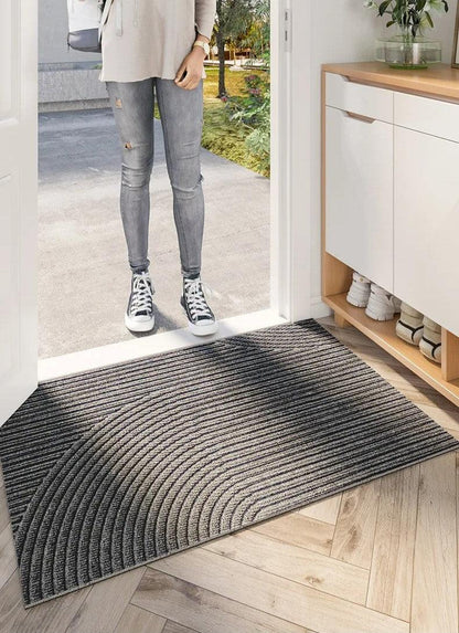 Person i jeans och gymnastikskor står utanför öppen dörr, framför en randig grå matta med böjt mönster på parkettgolv. 5