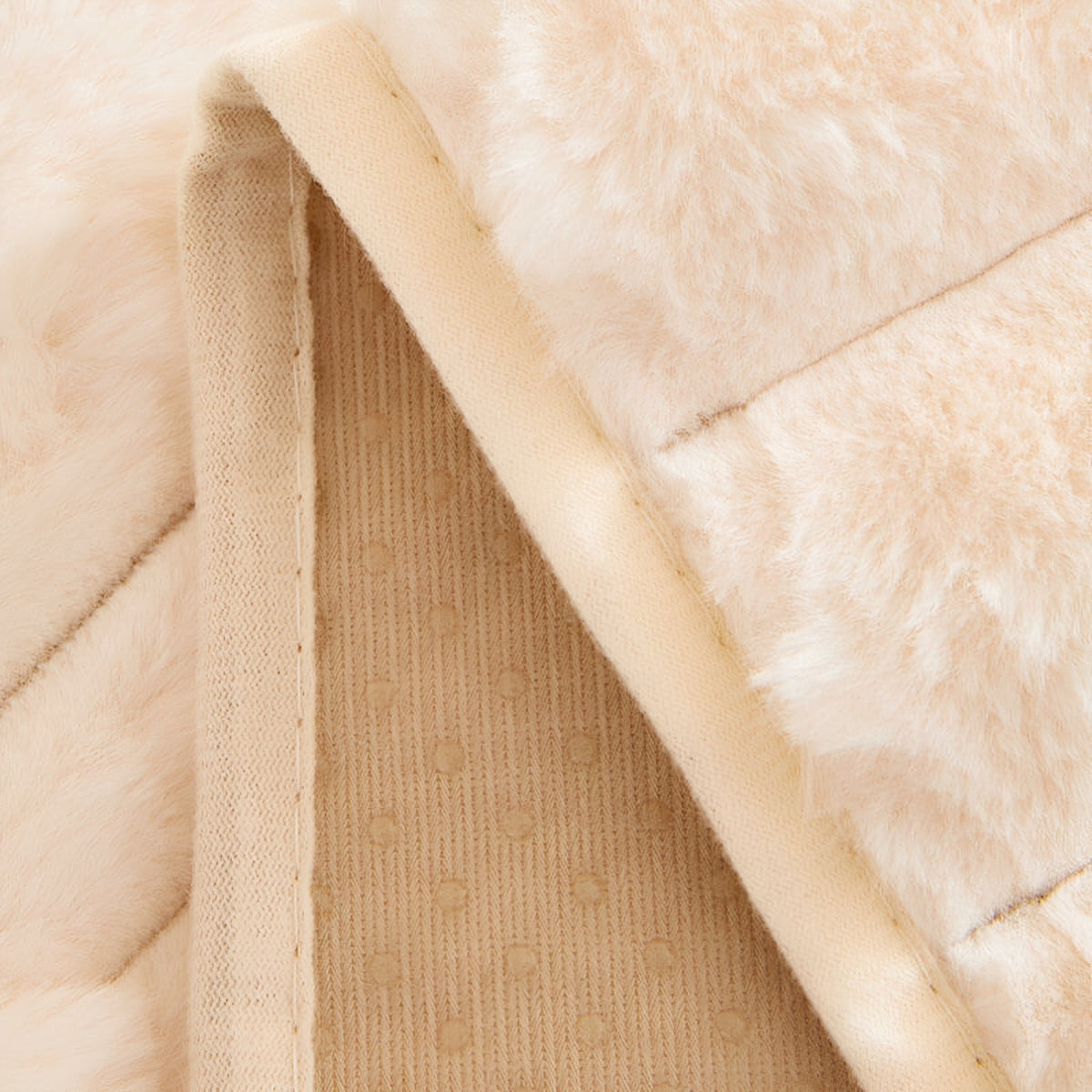 Detalj av överdragets avigsida i beige med prickigt halkskydd och sydd kant intill det mjuka plyschtyget. 6