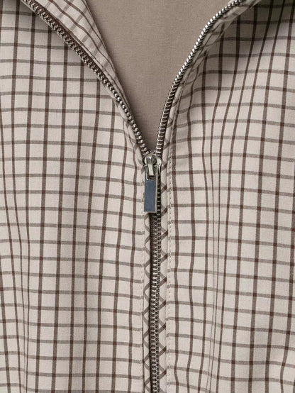Detaljbild av jackans dragkedja i silverfärg med skjutare mot rutigt tyg i beige och brunt. 6