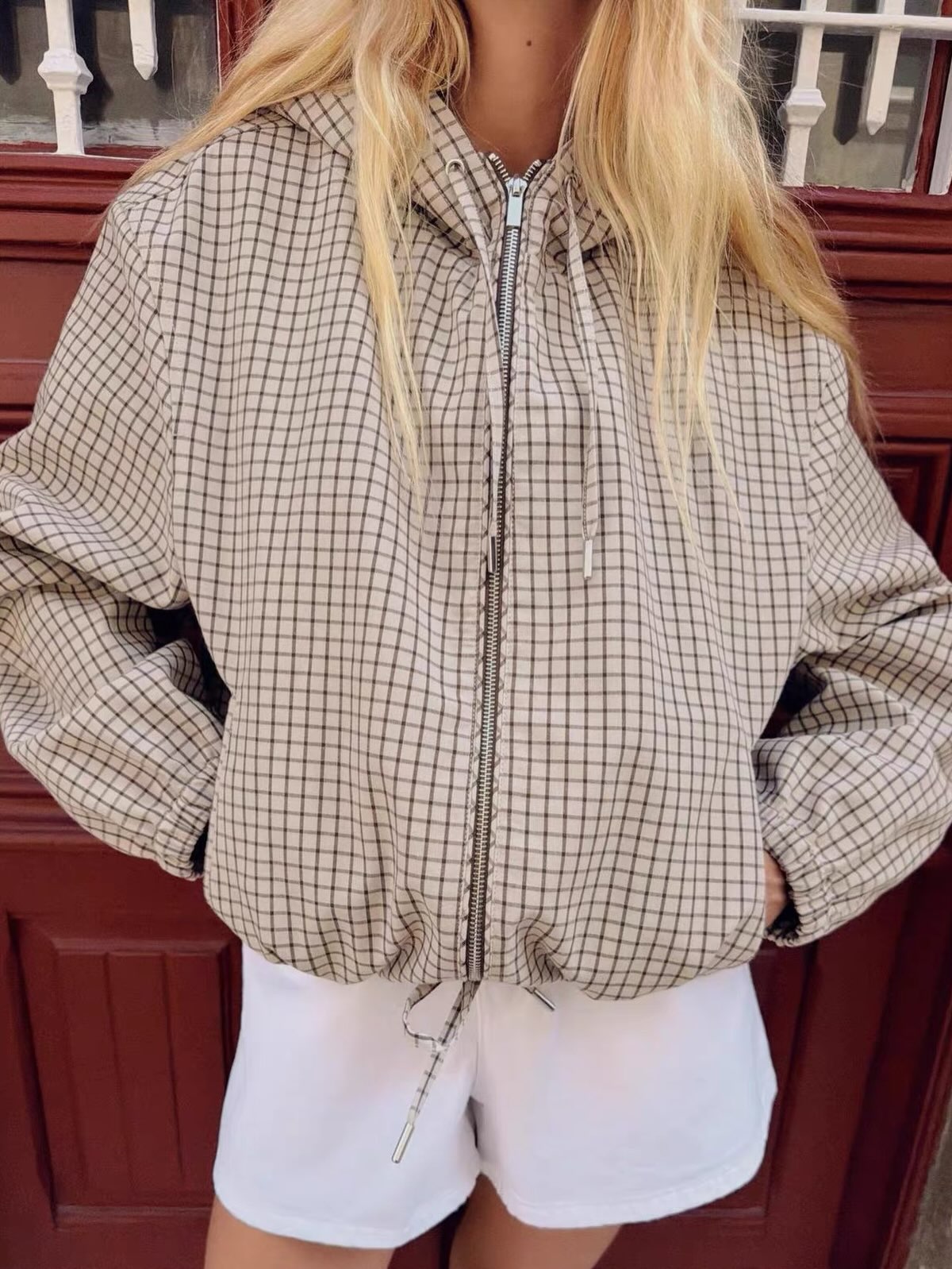 Närbild av jackans framsida på modell: rutigt tyg, dragkedja, dragsko vid huvan och dragsko i nederkant, händerna i fickorna. 3