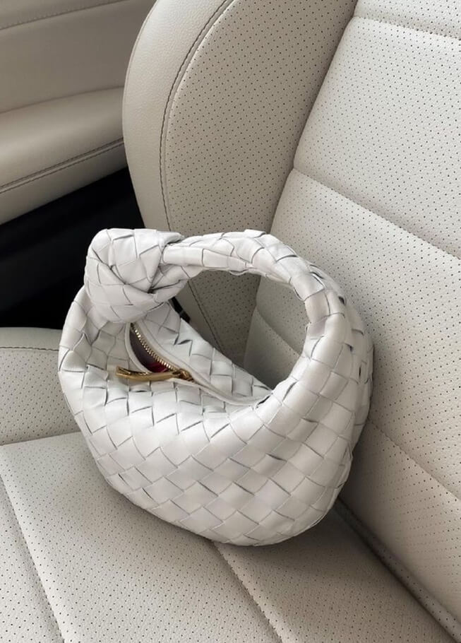 Weiße geflochtene Handtasche aus Leder auf Autositz, modisches Accessoire, Damenmode.