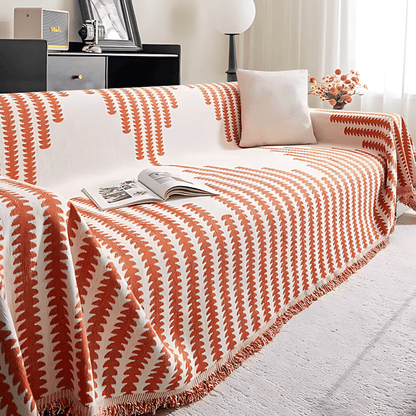 Överdraget i orange och krämvitt på soffan, med vit kudde, uppslagen tidning och blommor i bakgrunden. 7