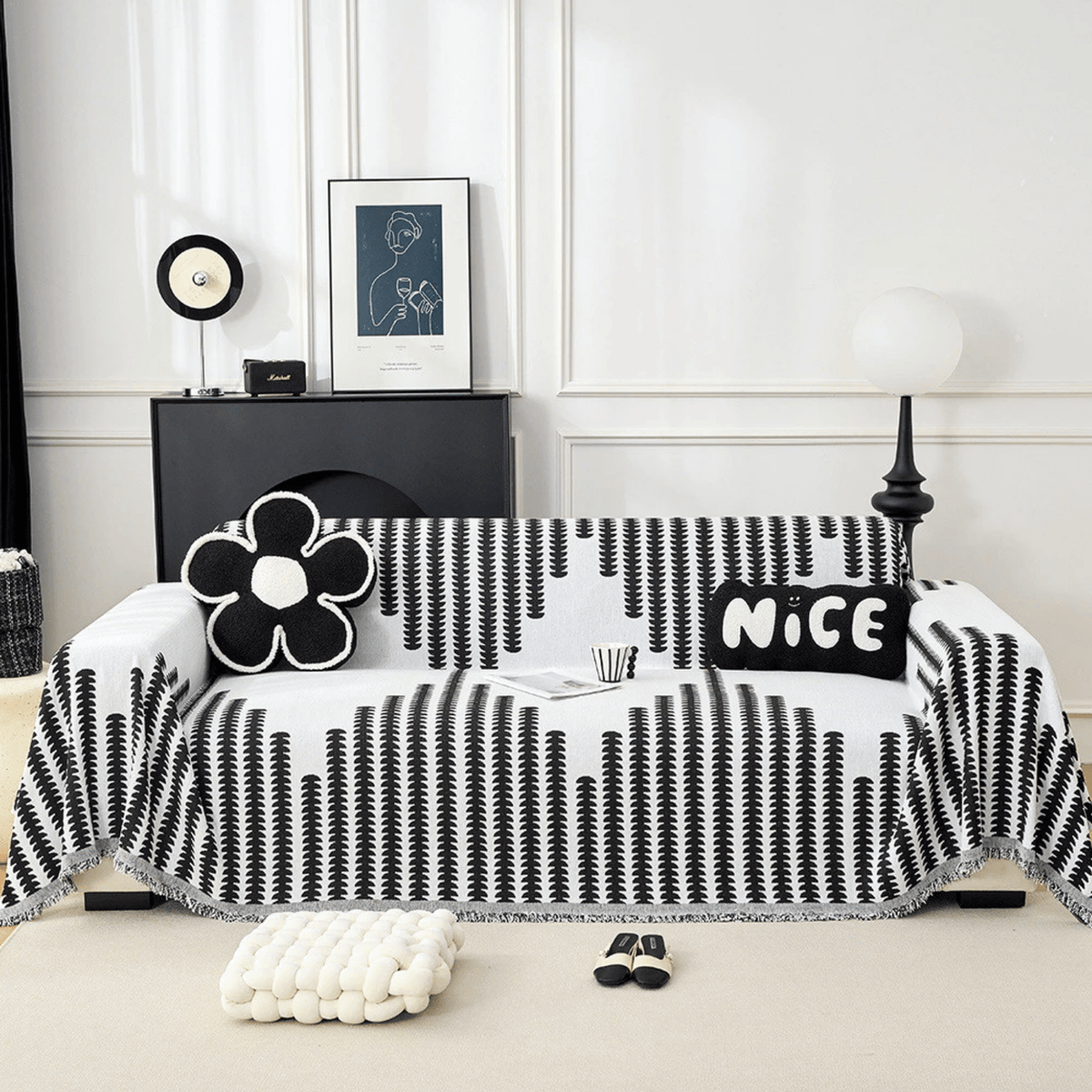Svartvitt överdrag med bladmönster draperat över en soffa, med blomformad och rektangulär kudde, sett rakt framifrån i ett ljust vardagsrum. 1