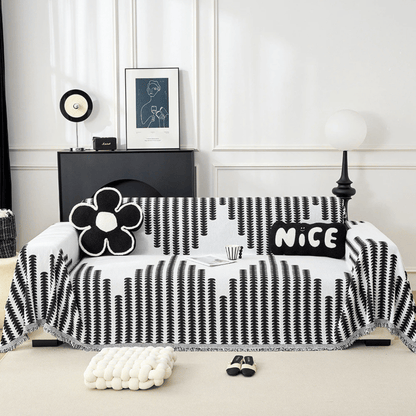 Svartvitt överdrag med bladmönster draperat över en soffa, med blomformad och rektangulär kudde, sett rakt framifrån i ett ljust vardagsrum. 1