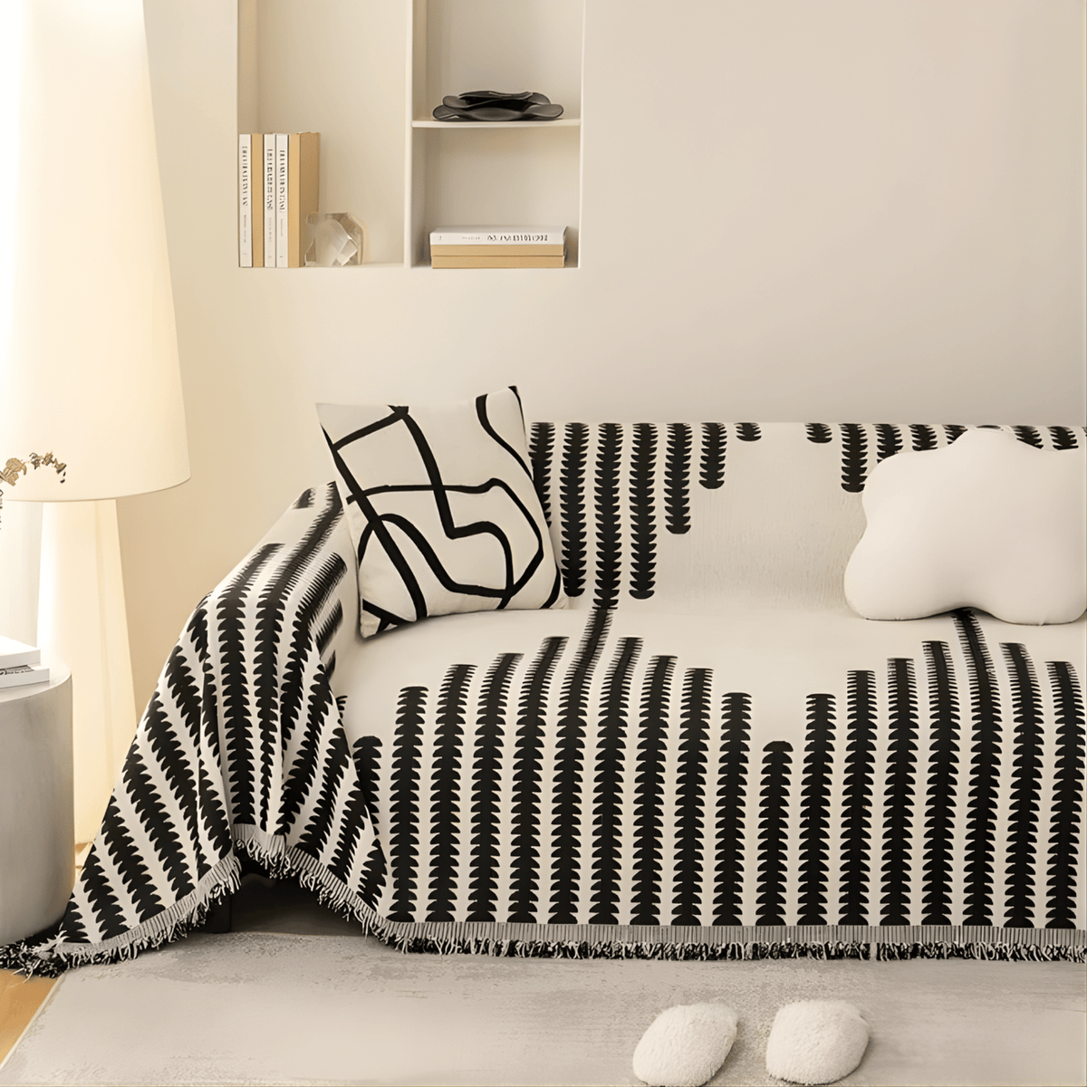 Överdraget i svart och krämvitt på en soffa i ett ljust rum, med mönstrad kudde, molnformad kudde och fransad kant. 3