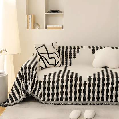 Överdraget i svart och krämvitt på en soffa i ett ljust rum, med mönstrad kudde, molnformad kudde och fransad kant. 3