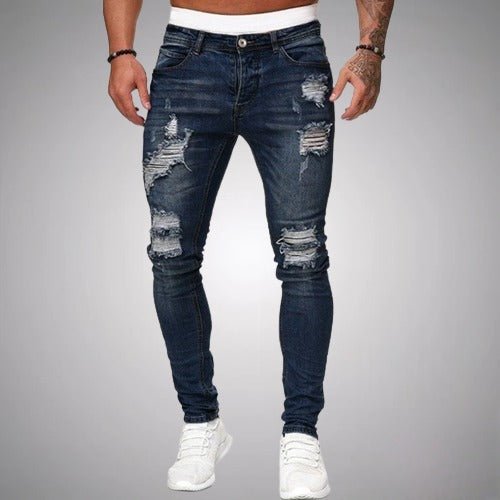 Man i mörkblå slitna slim fit-jeans med revor på lår och knän, framifrån, med vita sneakers. 4