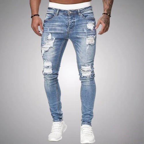 Man i ljusblå slitna slim fit-jeans med revor på lår och knän, framifrån, med vita sneakers. 2