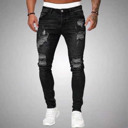 Man i svarta slitna slim fit-jeans med revor på lår och knän, framifrån, med vita sneakers. 1