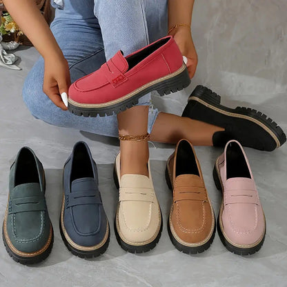 Loafers i sex färger, grön, blå, beige, brun, rosa, röd och svart, uppställda tillsammans medan en röd sko hålls upp. 2