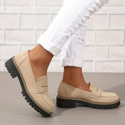 Beiga loafers med kraftig svart sula, burna med vita slitna jeans mot vit tegelvägg, sedda från sidan. 3