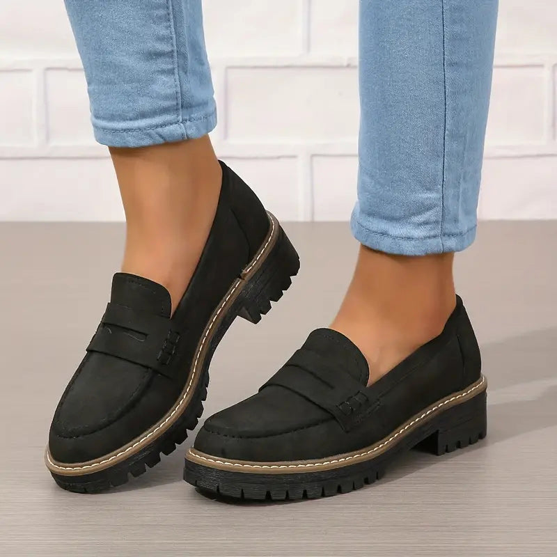 Svarta loafers med grov sula och kontrastsömmar, burna med uppvikta blå jeans mot vit tegelvägg. 6