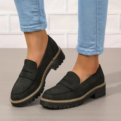 Svarta loafers med grov sula och kontrastsömmar, burna med uppvikta blå jeans mot vit tegelvägg. 6