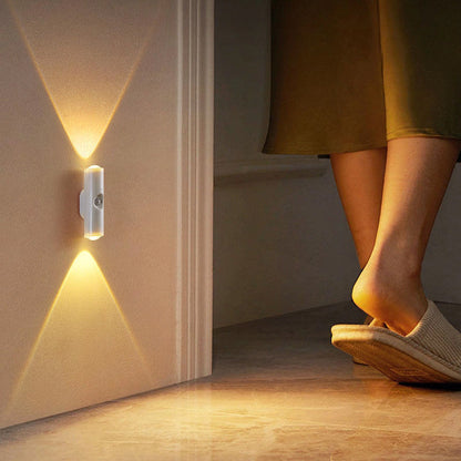 Vit vägglampa vid en dörröppning som lyser varmt, intill en kvinnas fötter i tofflor 13