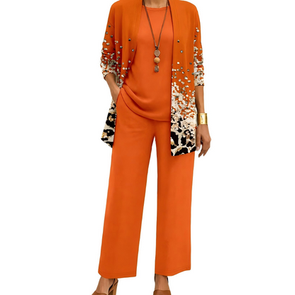 Modell i orange set där koftan har en prickig och leopardmönstrad nedre del, med matchande topp och vida byxor. 3