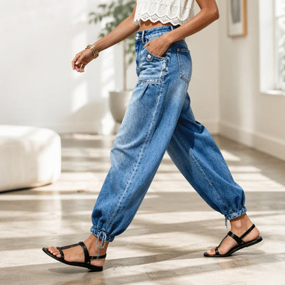 Sidovy av modell som går i blå jeans med knytband vid fållen och svarta sandaler i ett ljust rum. 7