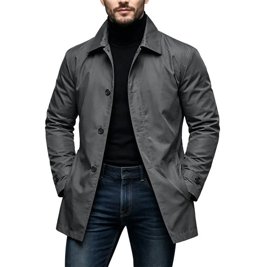 Man bär den gråa regnrocken framifrån med svart polotröja och jeans, händerna i fickorna 1