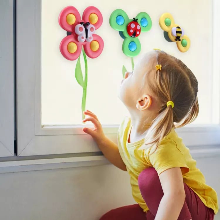 Kind spielt mit bunten Saugnapf-Spinnerspielzeug, Schmetterling, Marienkäfer, Biene am Fenster.
