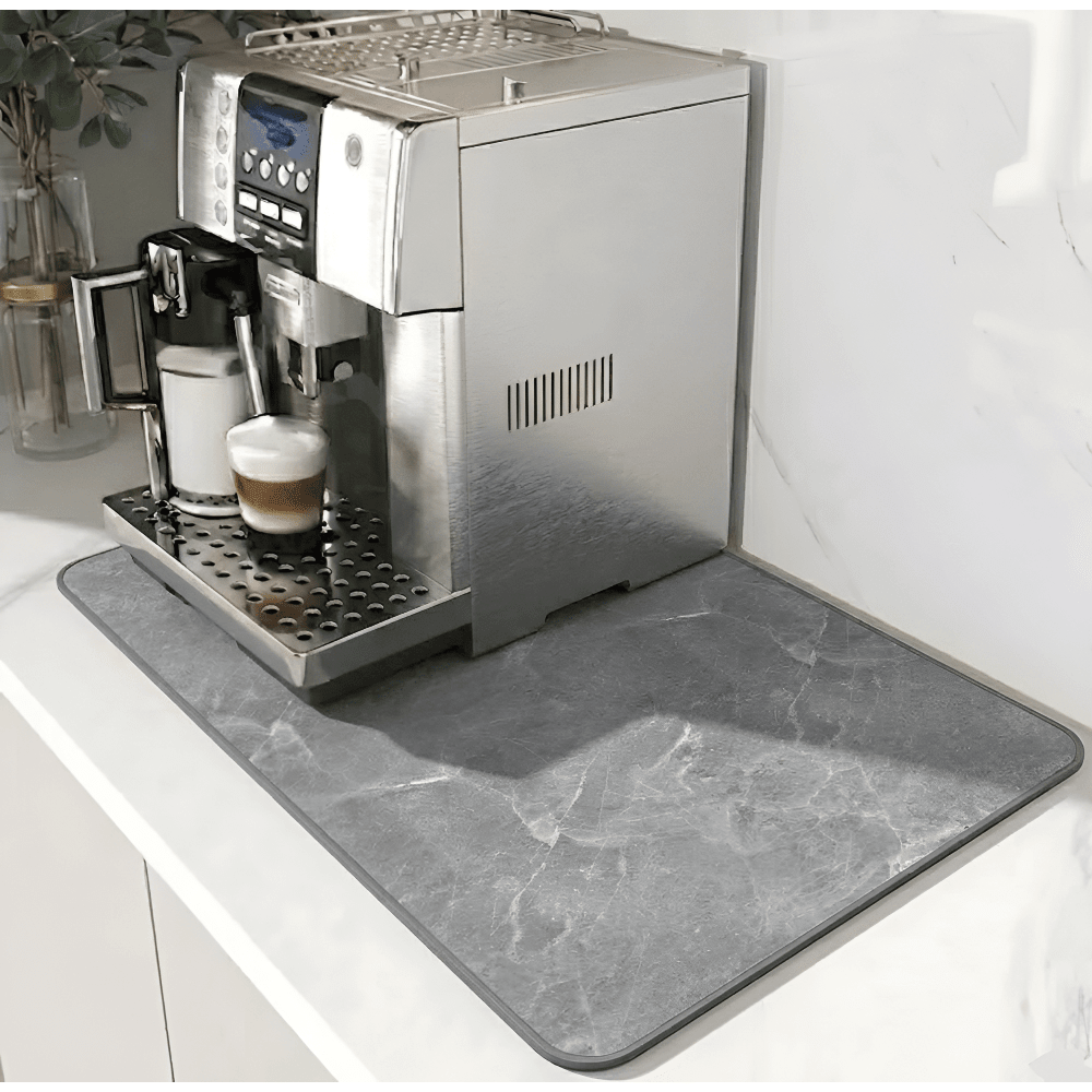 Grå marmormönstrad matta med mörkare kant under en silverfärgad kaffemaskin på en vit bänk. 12