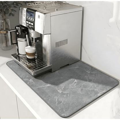 Grå marmormönstrad matta med mörkare kant under en silverfärgad kaffemaskin på en vit bänk. 12