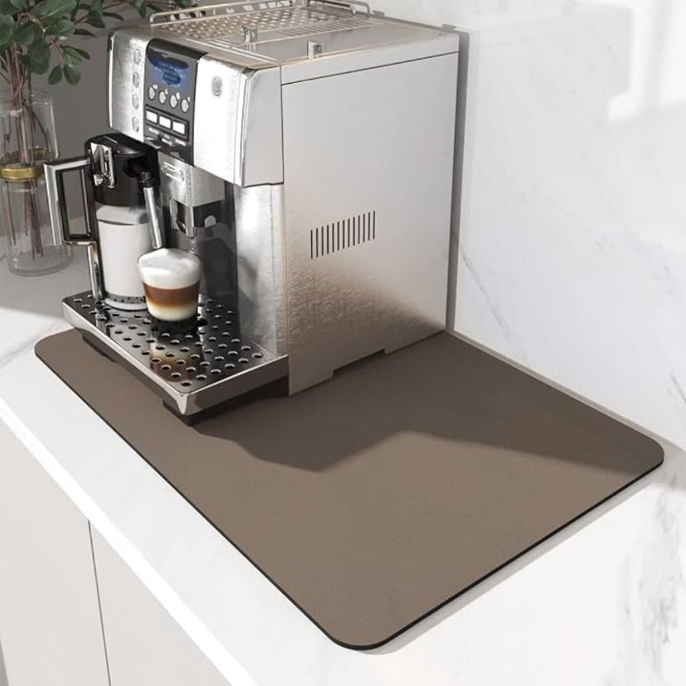 Brungrå matta under en silverfärgad kaffemaskin på en vit bänk, med ett glas latte som fylls på. 3