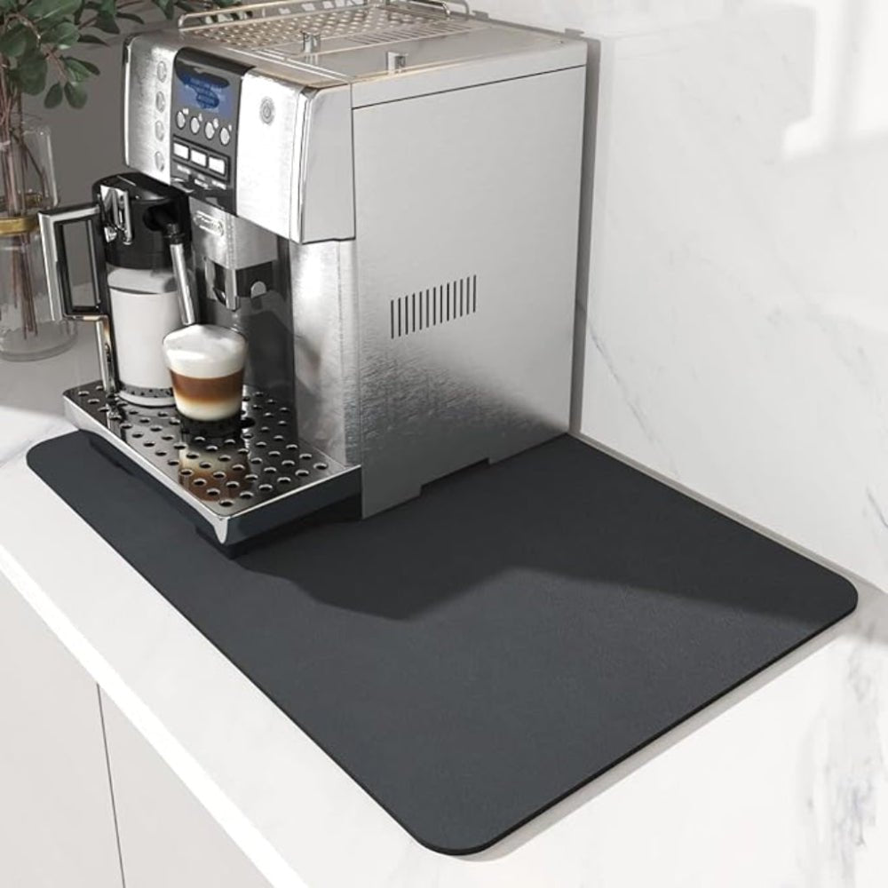 Mörkgrå matta med rundade hörn under en kaffemaskin på en vit marmorbänk, med en latte på droppgallret. 2