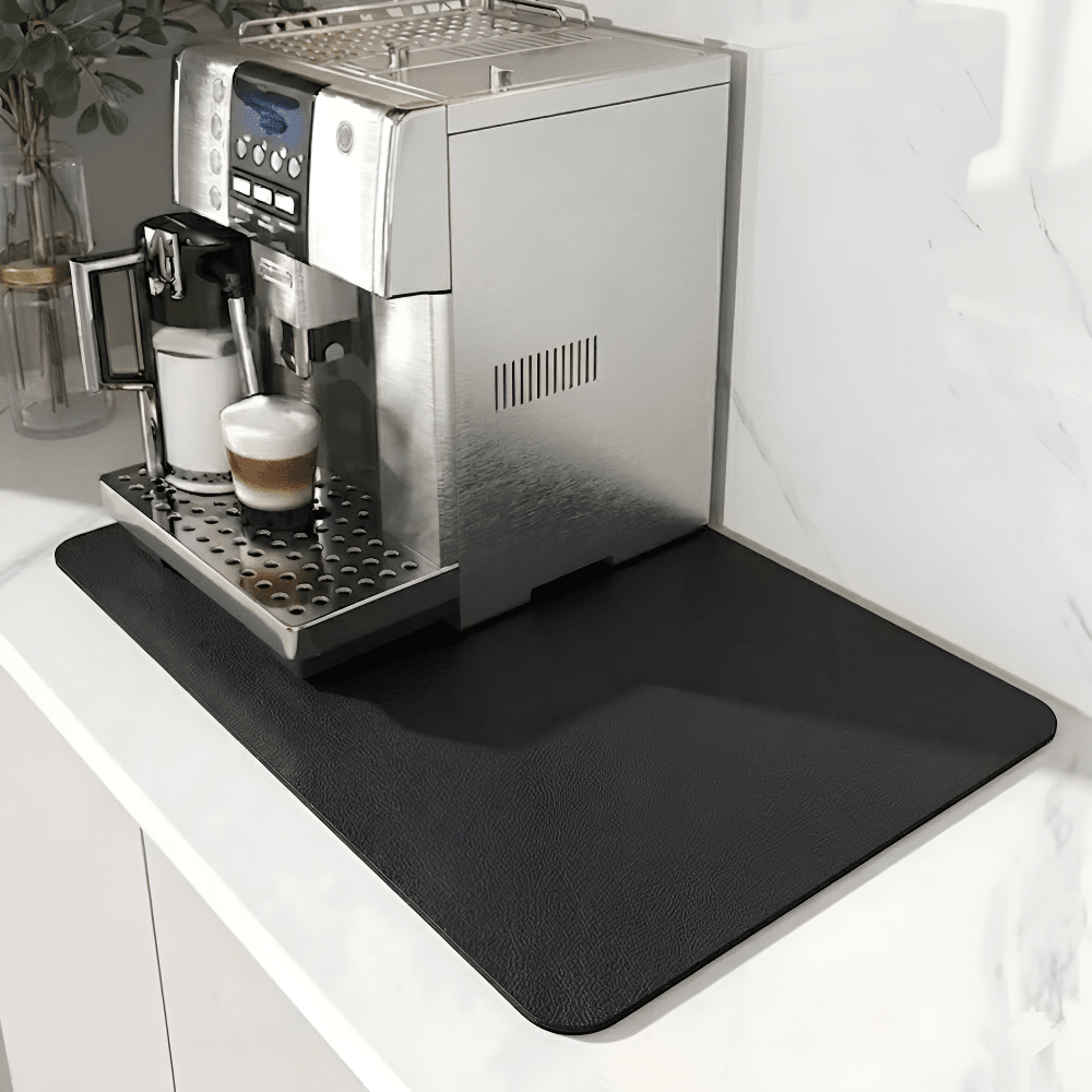 Svart matta med lätt texturerad yta under en silverfärgad kaffemaskin på en vit marmorbänk. 9